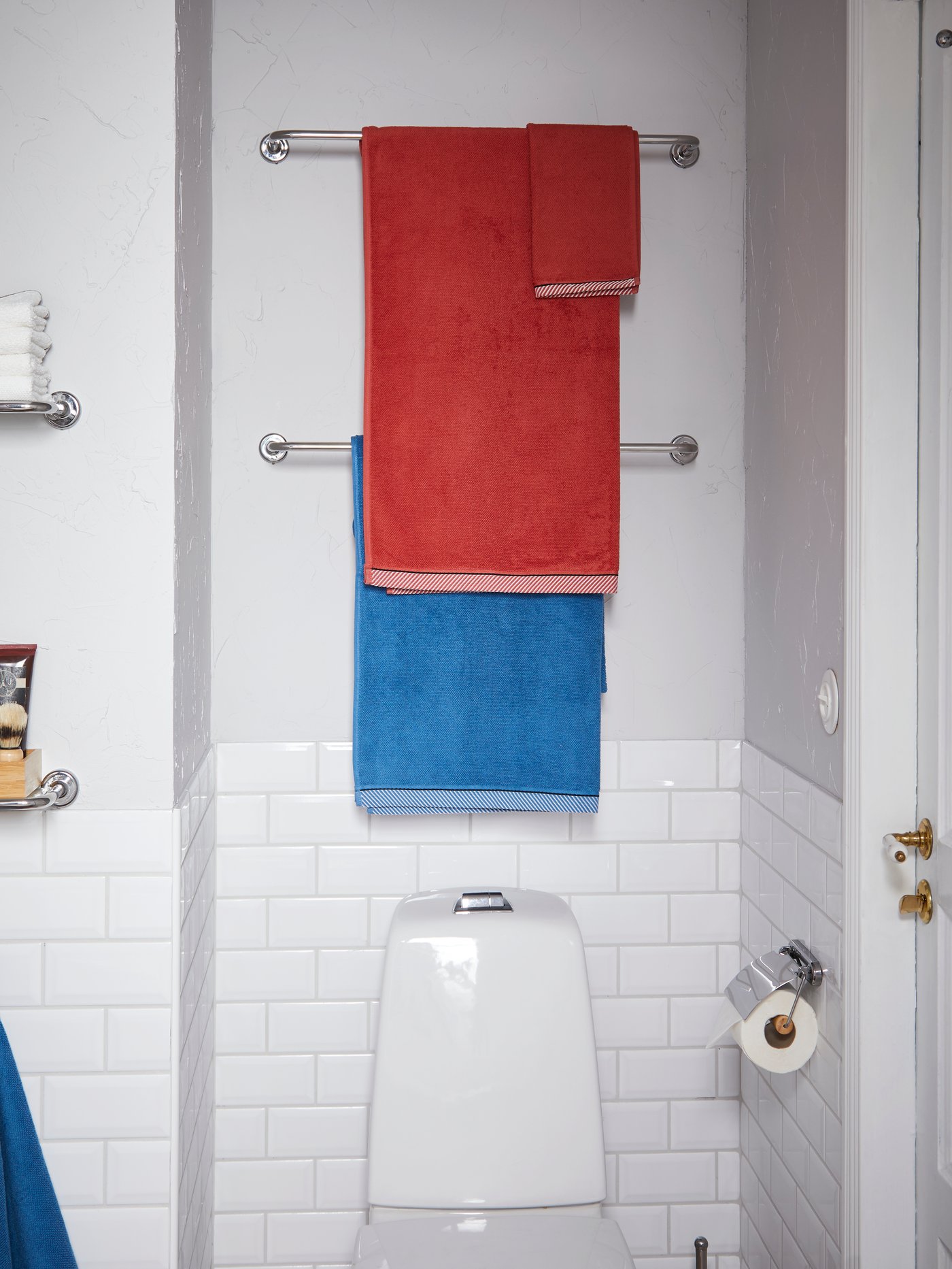 Two VOXNAN towel rails in chrome effect are placed on the wall over the toilet and bathroom towels hang on them.