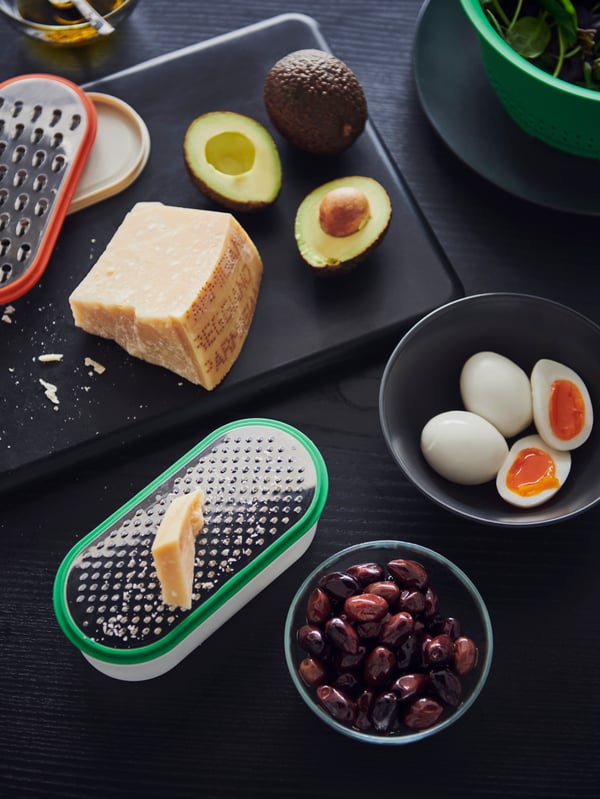 UPPFYLLD graters in different colours, some avocados and cheese and a FÄRGKLAR bowl and a GLADELIG bowl with food.