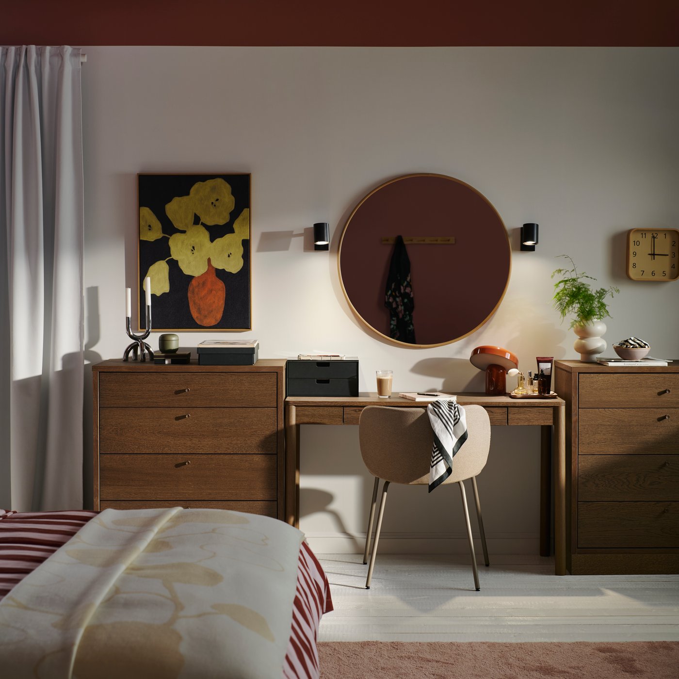 A bedroom with a desk between two dark brown TONSTAD chests of 4 drawers with items on top and a round mirror on the wall.
