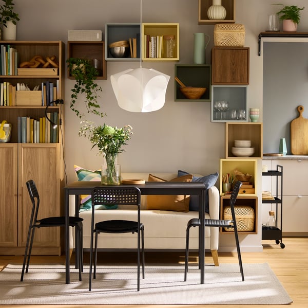 A black SANDSBERG table, three chairs and a sofa are placed in a living room with a BILLY bookcase in the background.