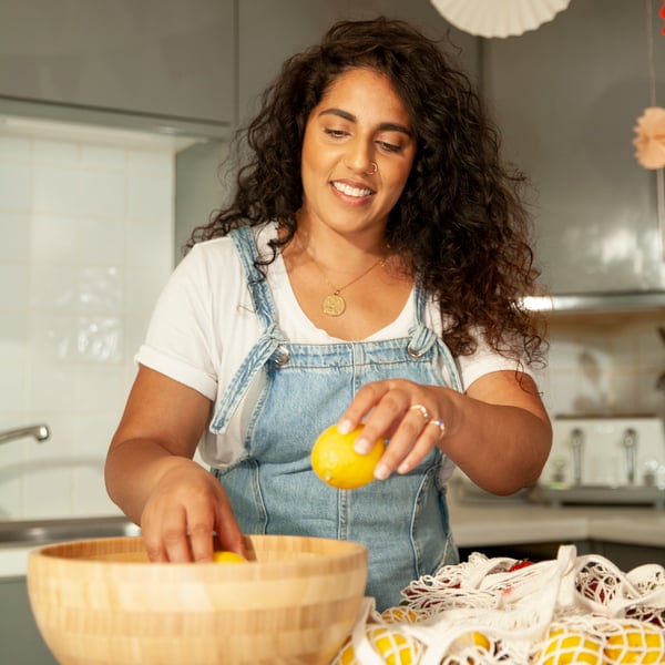 Woman taking lemons out of KUNGSFORS reusable shopping bag and put them into BLANDA bamboo bowl