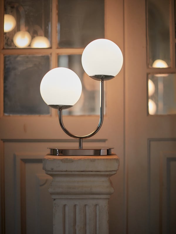 A SIMRISHAMN floor lamp in the corner of a living room with hessian wall covering, a rust sofa and a leafy green plant.