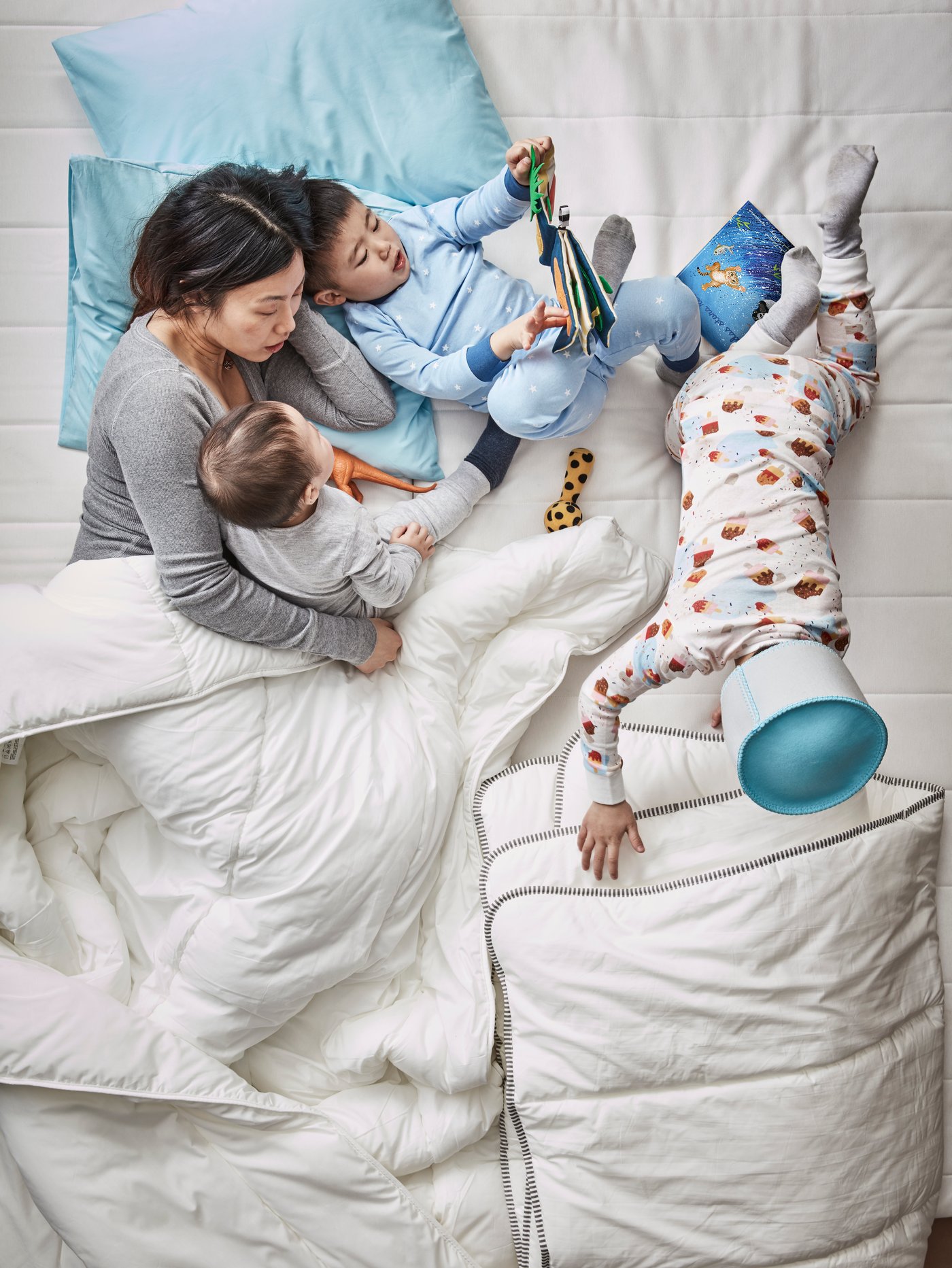 A mother and three children lie in a bed with blue pillows and white duvets reading a DJUNGELSKOG picture book.