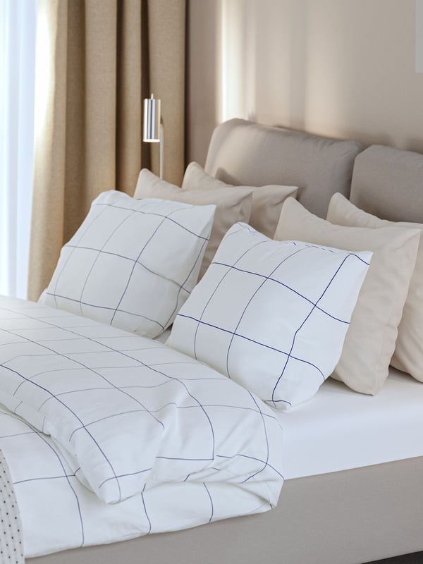 Una camera d'albergo con un letto imbottito SAGESUND realizzato con biancheria BREDVECKLARE accanto a un comodino impiallacciato in rovere.