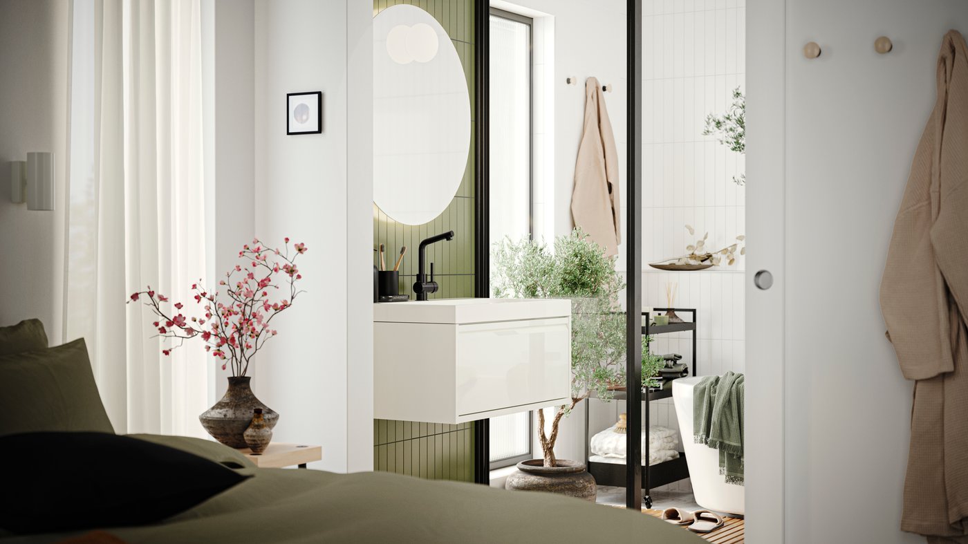 A bathroom with an ÄNGSJÖN wash-stand with drawer in high-gloss white, a mirror and a bathtub seen from a bedroom.