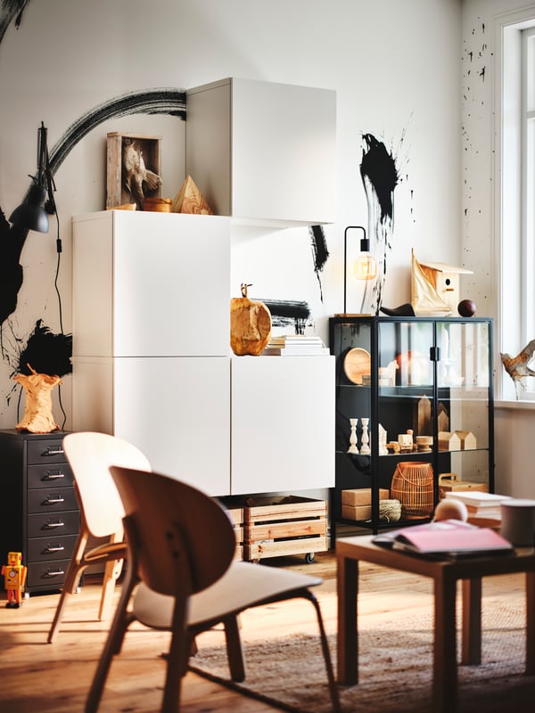 White BESTÅ shelf units with doors are mounted on a wall. Two FRÖSET easy chairs and a LACK side table are arranged near it.
