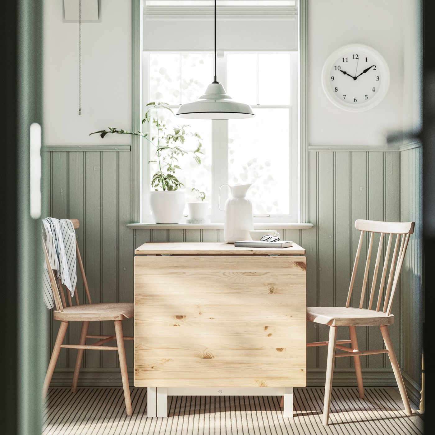 A light brown stained/white stained PINNTORP gateleg table is placed below a kitchen window with two HÖGVED chairs.