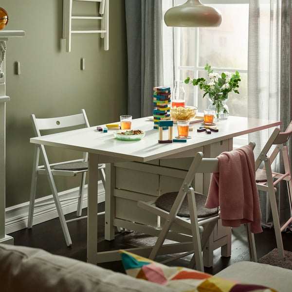 White NORDEN rectangular gateleg table with 3 foldable chairs in a pastel green dining room by the full-length window.