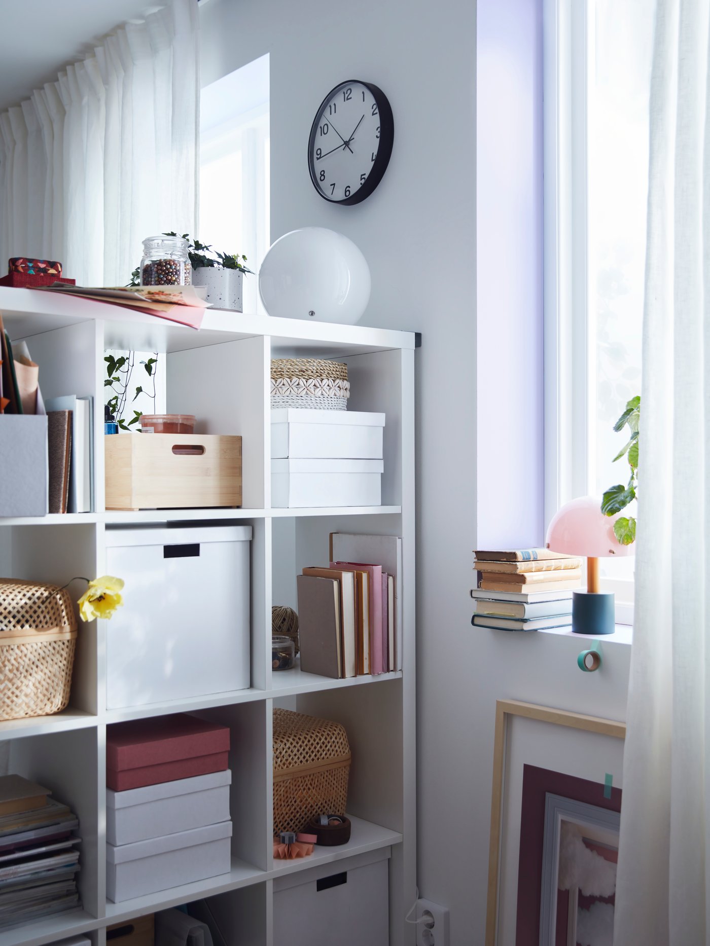 En rumsindelande vit KALLAX placerad vinkelrätt mot en ljus vägg och fylld med böcker, lådor och accessoarer.