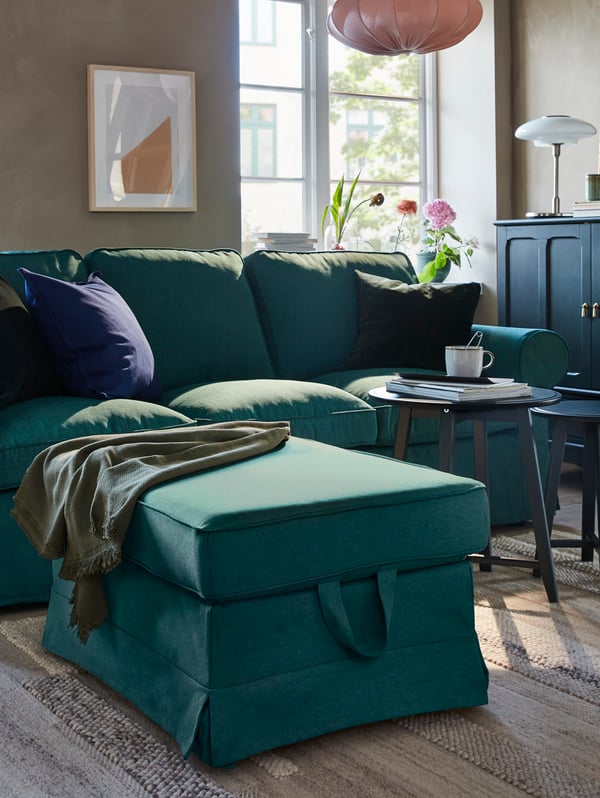 Un canapé et un repose-pieds turquoise foncé, deux tables gigognes bleu-vert foncé, un tapis et une armoire bleu-vert foncé.