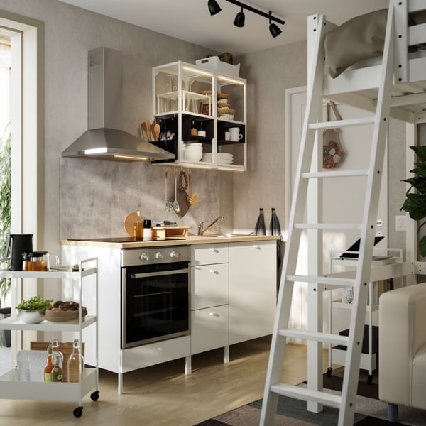 An open kitchen has white ENHET open frames and base cabinets with white doors and there’s a loft bed in the foreground.