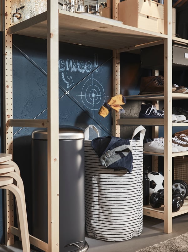 Une grande poubelle à pédale et un sac à lessive KLUNKA sur le sol sous une tablette dans un grand rangement IVAR en bois.