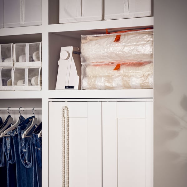 Zwei PÄRKLA Taschen liegen in einem Regal, unter dem sich ein weißer BRIMNES Kleiderschrank mit 2 Türen befindet.