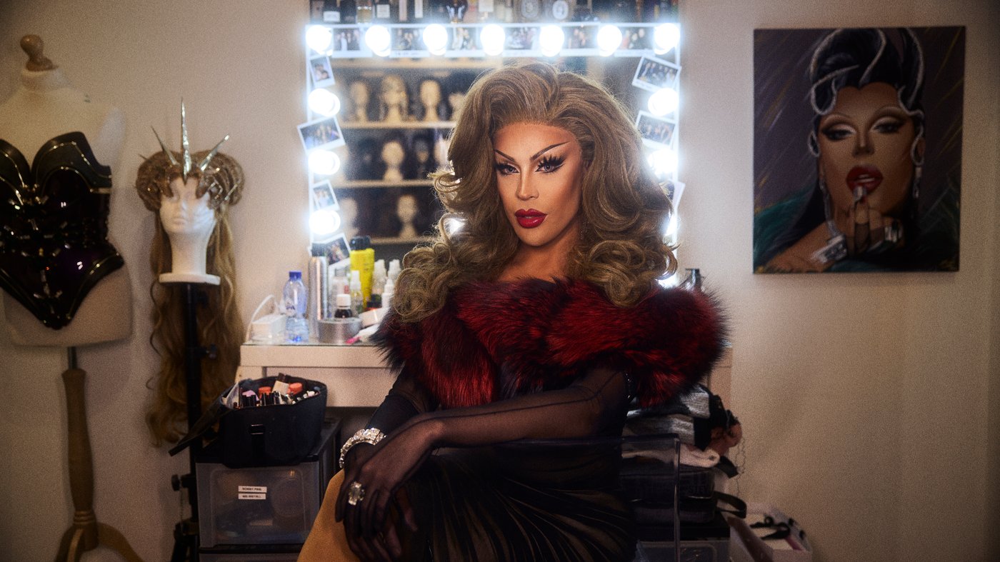 Envy Peru in full make up and dressed up in drag, sitting in front of her vanity mirror in the dressing room.