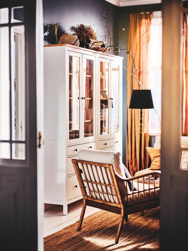 Two white HEMNES glass-door cabinets with three drawers, with four TVÄRDRAG cabinet lights on top, and an armchair on a rug.