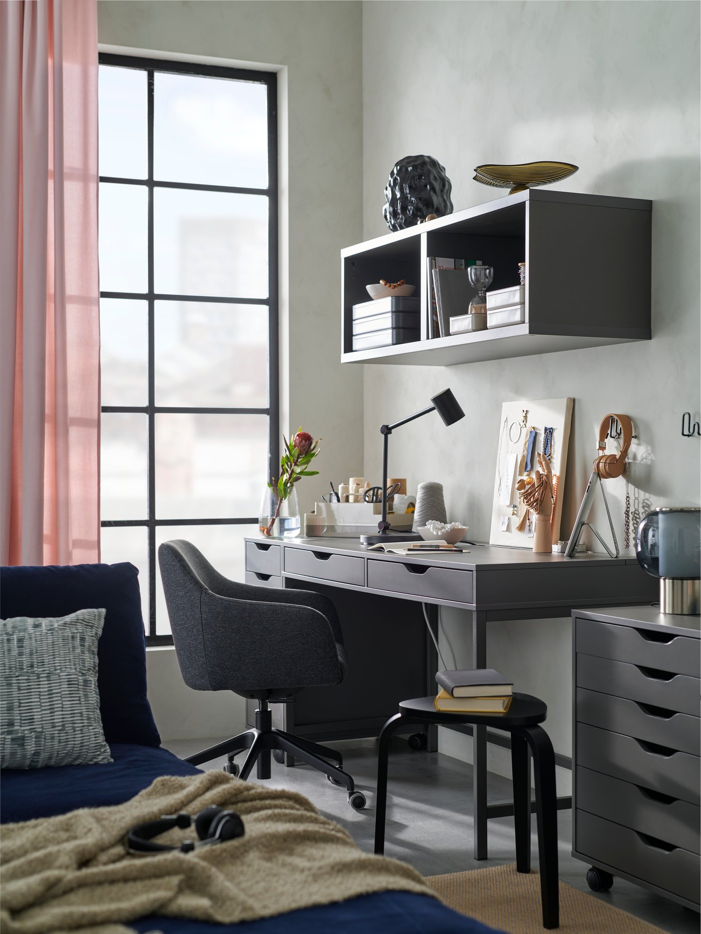 A living room hobby area with a TOSSBERG/LÅNGFJÄLL conference chair next to a dark grey ALEX desk and storage units.