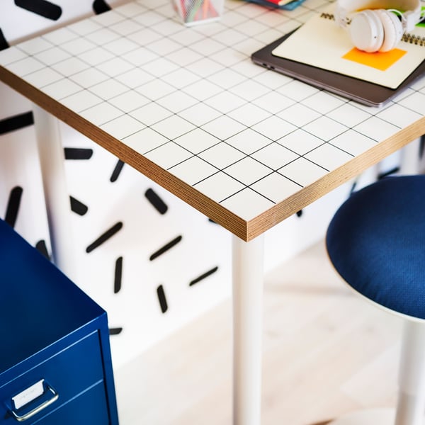 A white-and-birch LAGKAPTEN desk, its top tilted and with dried plants on paper on top and a white spotlight clamped to it.