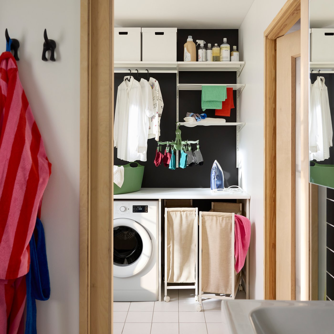 Combinación BOAXEL blanca y metálica para lavandería, con repisas, riel para ropa y soluciones de almacenamiento sobre una lavadora.