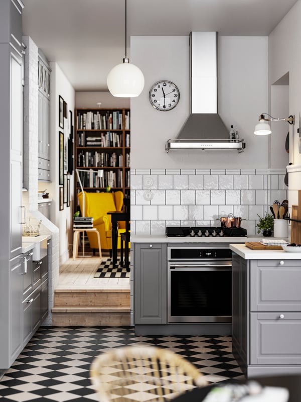 A kitchen with a chequered floor, grey BODBYN fronts with off-white/chrome plated handles and knobs, plus a pendant lamp.