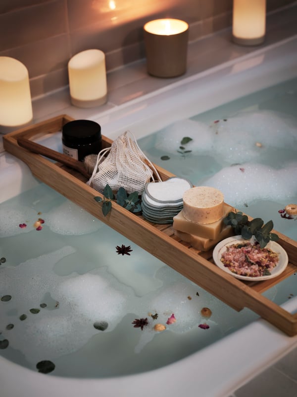 Badewanne mit Wasser und Schaum, Holzablage mit Kerzen, Gläsern und getrockneten Blumen – entspannende Spa-Atmosphäre im Badezimmer