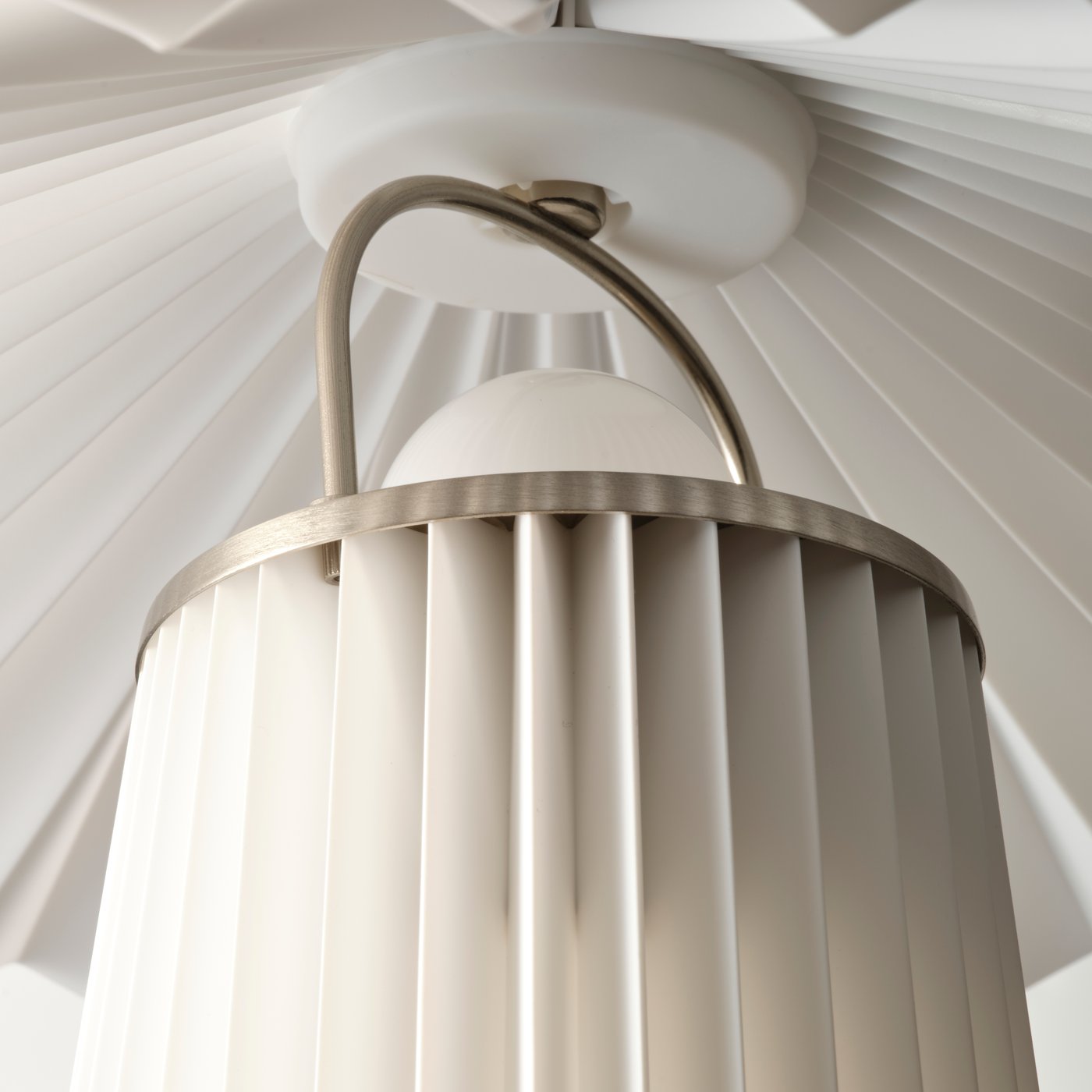 Insidan av en vit KUDDLAVA bordslampa, där ljuset spelar i veckningen på den runda lampskärmen runt en central björkknopp.