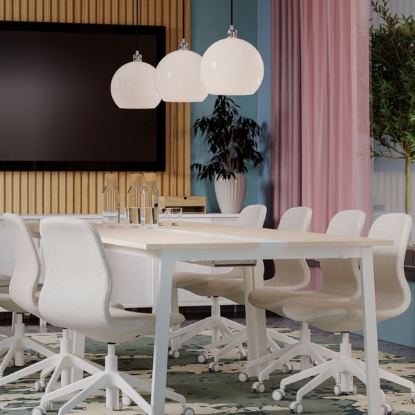 A modern meeting room has two birch veneer/white MITTZON conference tables and beige conference chairs by a large TV screen.