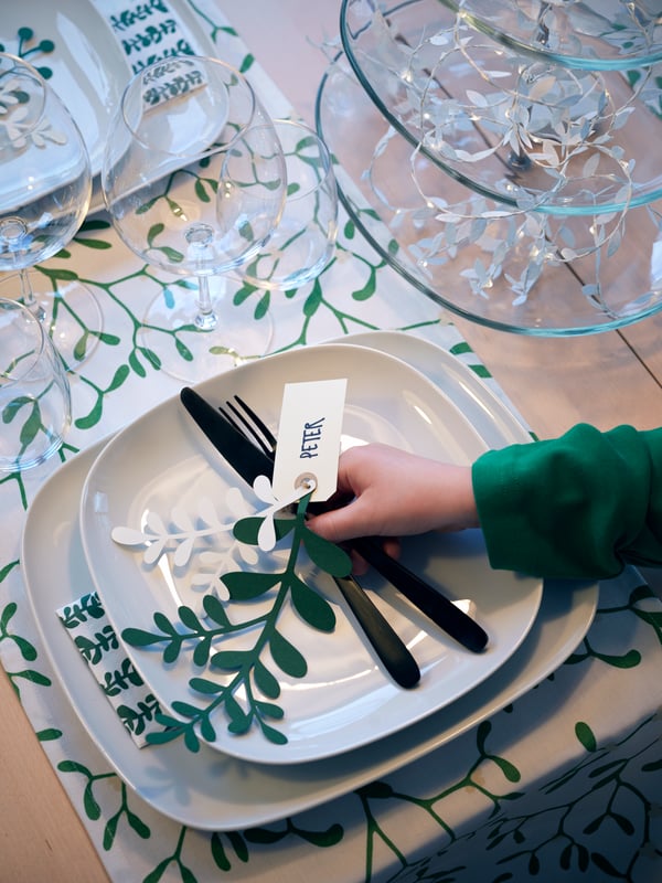 La mano de un niño colocando una etiqueta con su nombre sobre unos platos blancos.