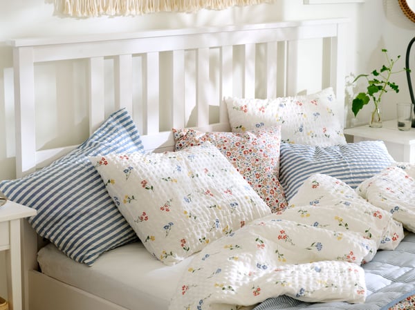 Close-up of a white HEMNES bed made with PILDVÄRGMAL duvet cover and pillowcases and bedding in other light colours.