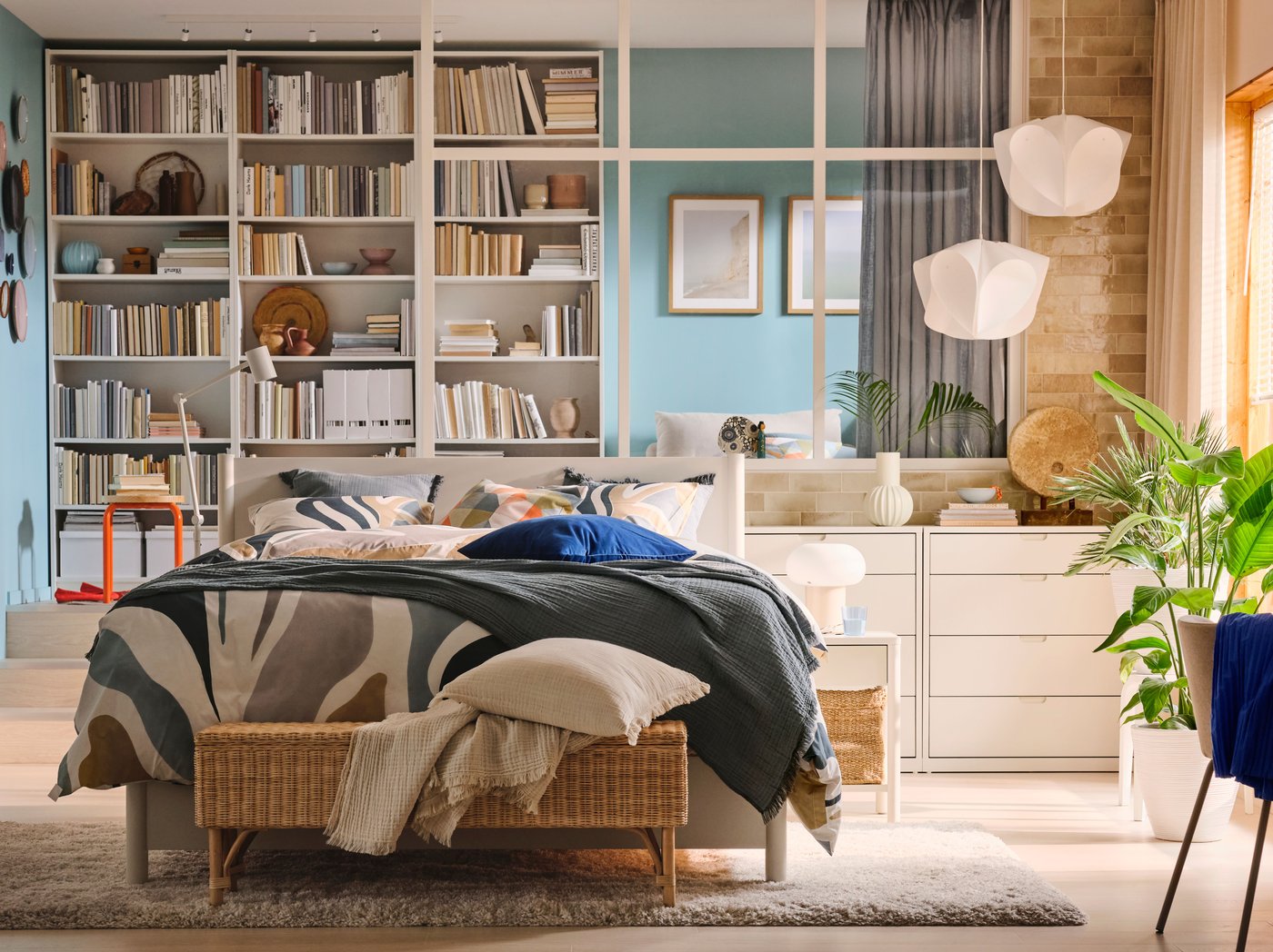 Una cama TONSTAD color hueso, vestida de ropa de cama MYGGLASVINGE en una recámara amplia delante de tres libreros BILLY blancos.