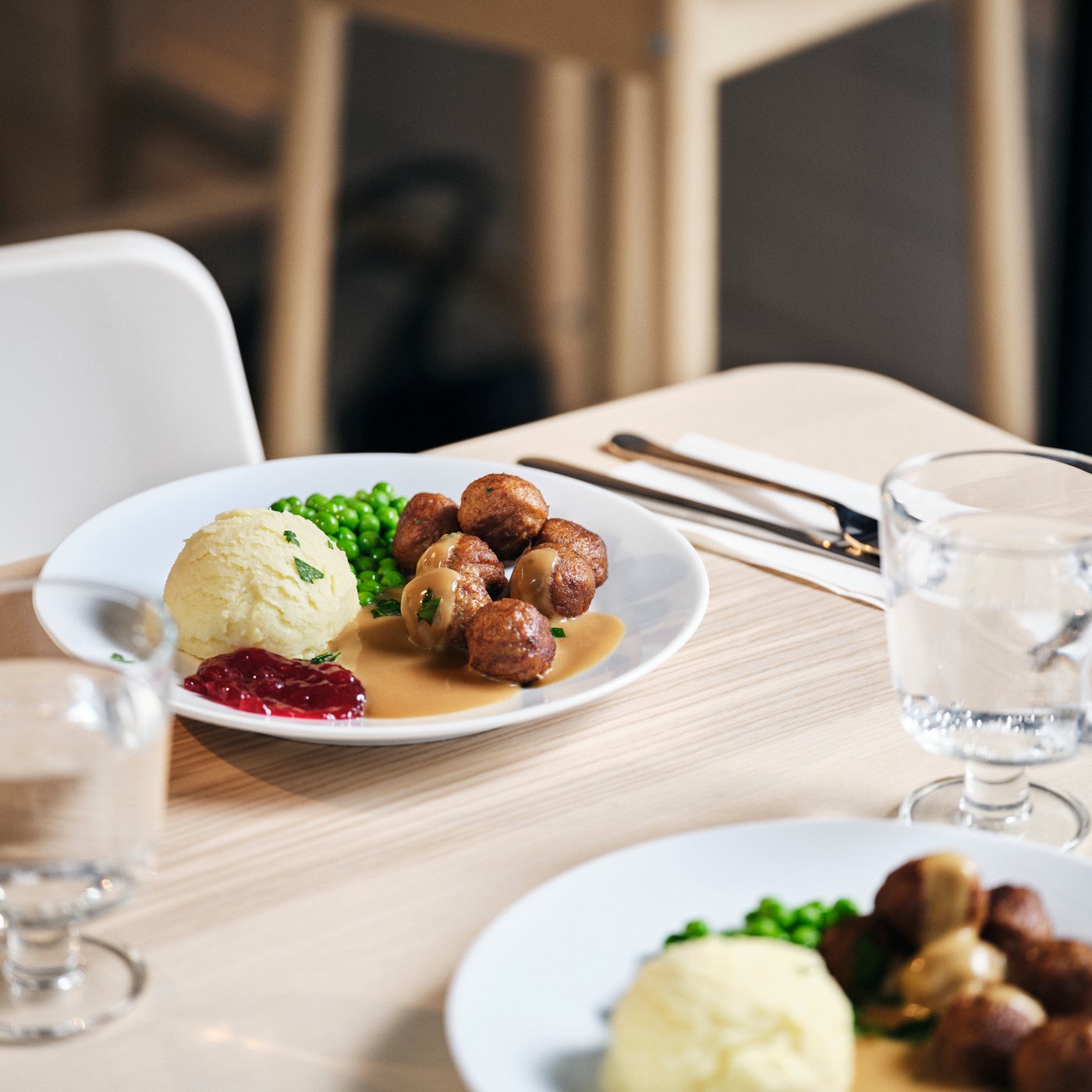 A plate of traditional Swedish meatballs with mashed potatoes, cream sauce, lingonberry jam, and green peas on a wooden table.