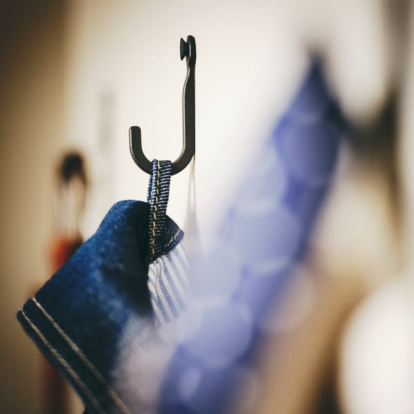 A denim item of clothing hanging from a HÖGAFFEL wall hook which has been fixed to a light beige wall.
