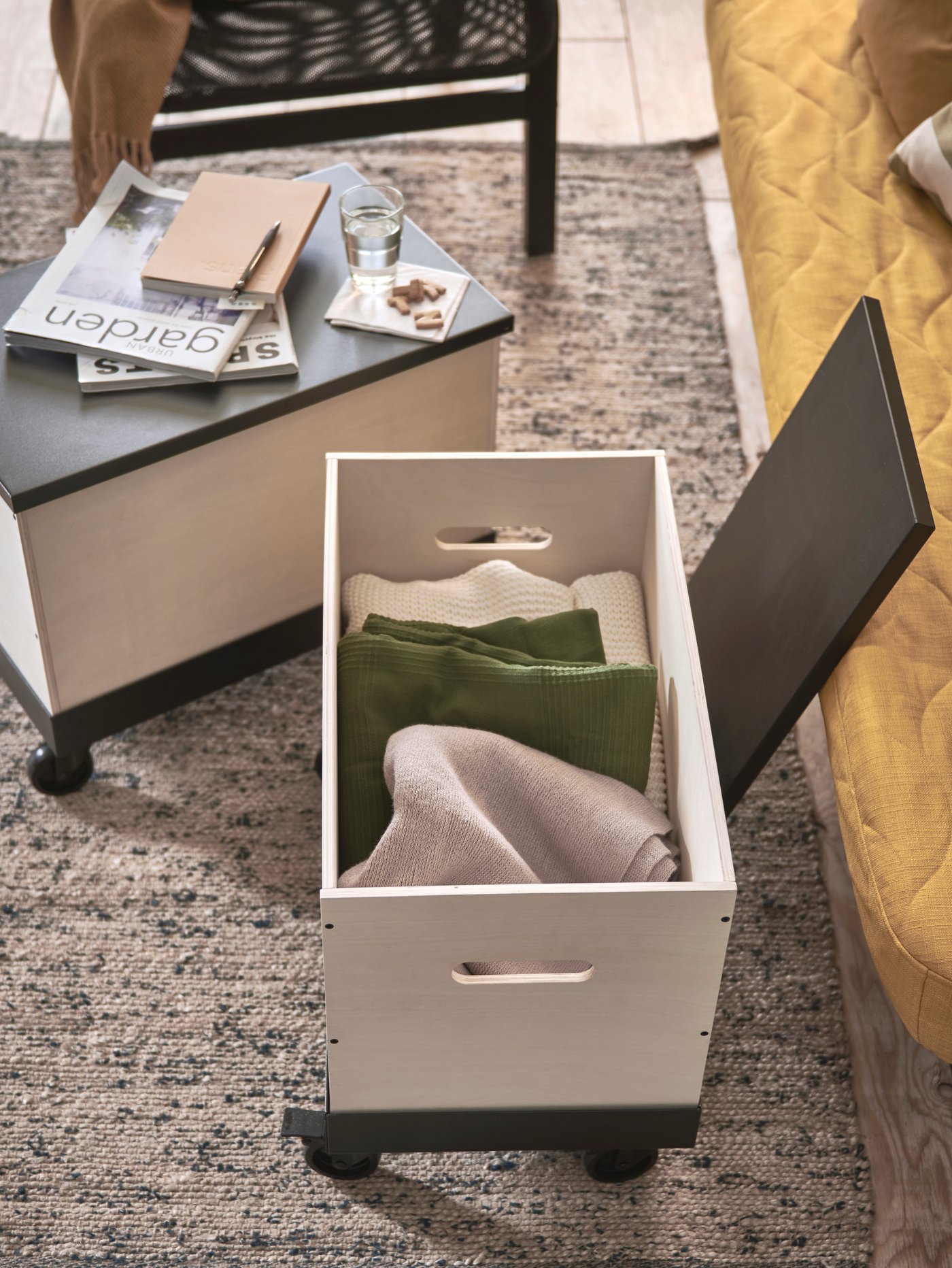 Two coffee/side tables on wheels made in birch plywood, with one of the tables opened up showing stored blankets inside.