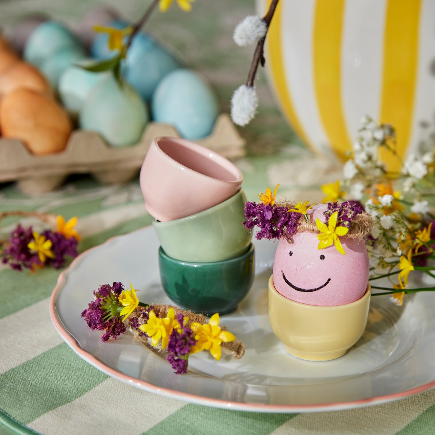 Een paasei beschilderd als een smiley, in een pastelkleurig IKEA 365-eierdopje op een UPPLAGA-bord.