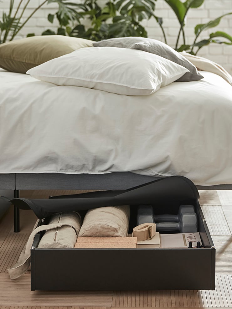 A neatly organised VARDÖR bed storage box pulled out from under a bed with ÄNGSLILJA quilt covers and three cushions.