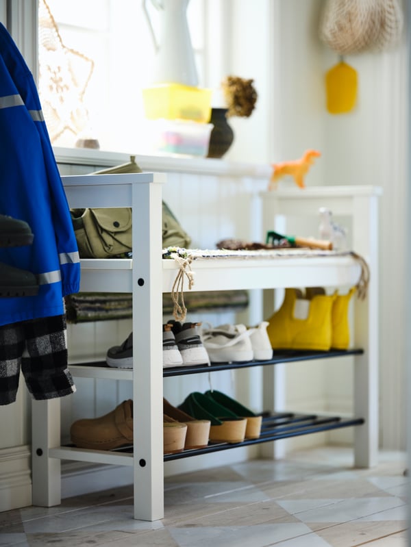 Dans un hall d’entrée, banc avec rangement pour chaussures HEMNES blanc ont sont rangées des chaussures et bottes de différentes couleurs.