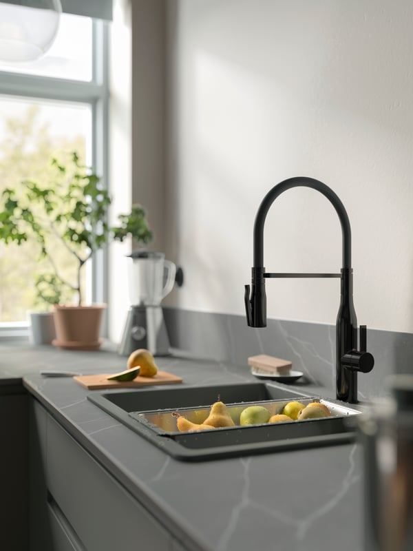 A colander filled with pears and apples is placed in a grey sink with a TOLLSJÖN kitchen mixer tap in black polished metal.