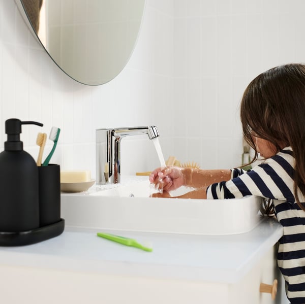 Un niño utiliza el grifo monomando para lavabo con sensor BROGRUND, con jabón y un cepillo verde visible en la encimera.