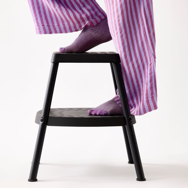 A person in purple and white striped trousers and purple socks is stepping onto a HADDARP step stool in 4-way black-grey.