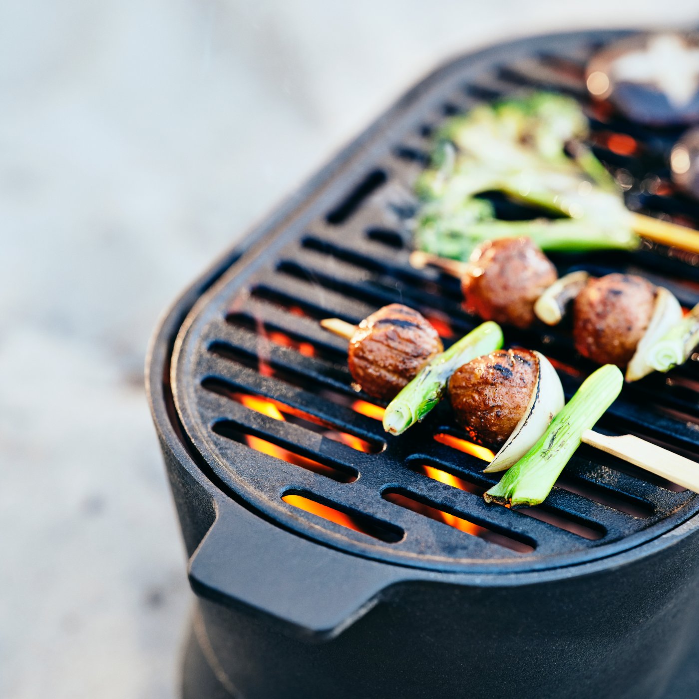 Skewers of HUVUDROLL plant balls and vegetables are grilling on a SOLUPPGÅNG barbecue.