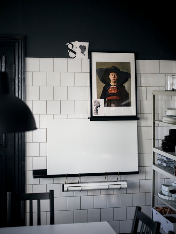 Art and an extra table held by black picture ledges on a white wall, the table legs in black HULTARP kitchen-roll holders.