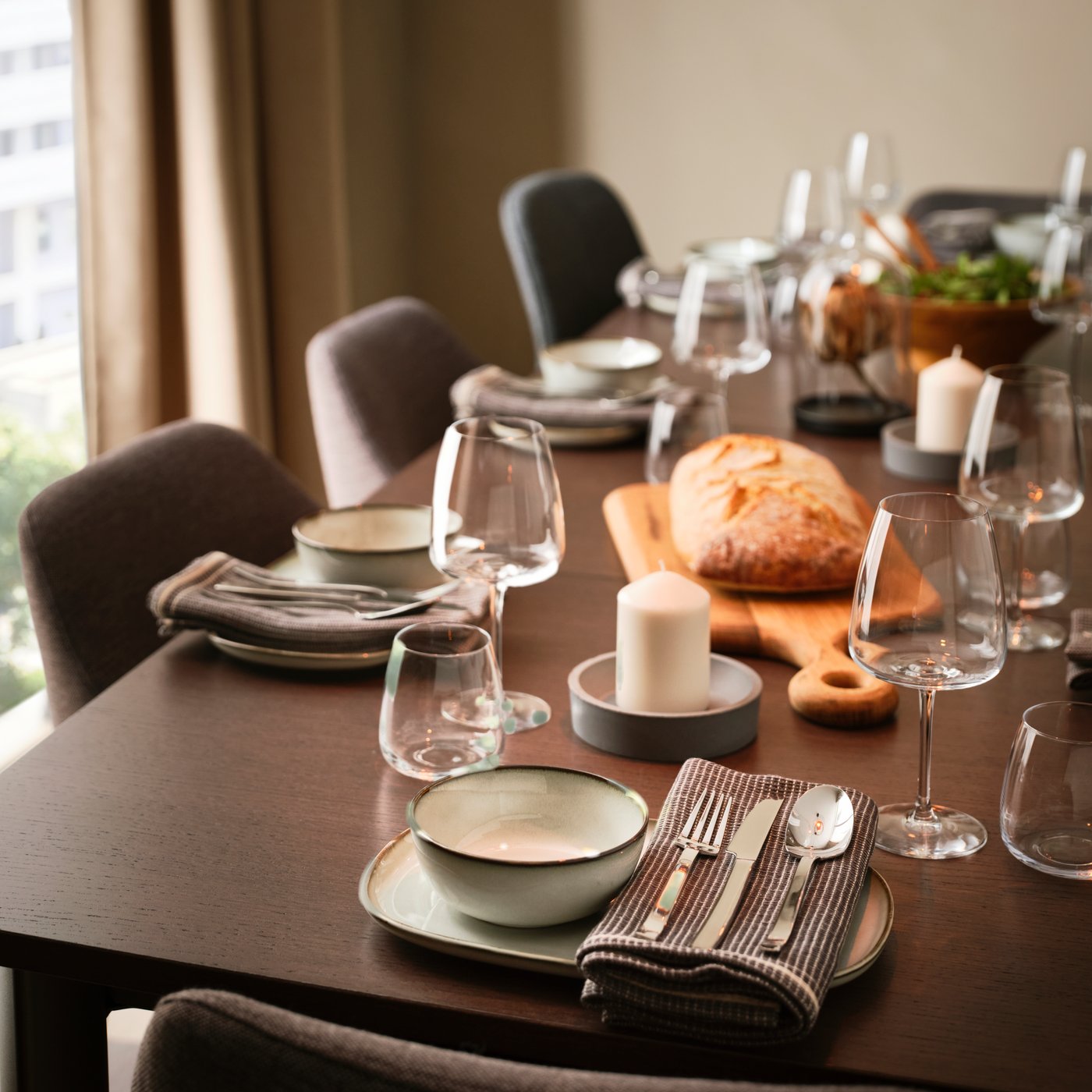 A table has a fancy table setting with plates, bowls and napkins with cutlery and DYRGRIP red wine glasses and water glasses.