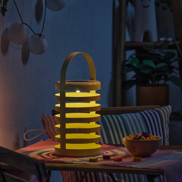 In a cosy outdoor setting shines a SOLVINDEN LED decorative table lamp in light green, next to a bowl of candy.