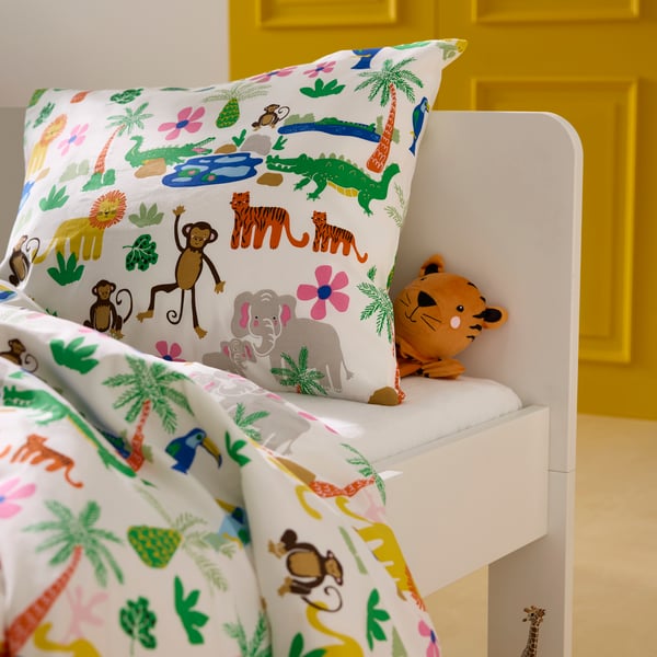 Nahaufnahme von einem weißen Kinderbett mit bunter Dschungel-Bettwäsche und einem Tiger-Handpuppenfreund.