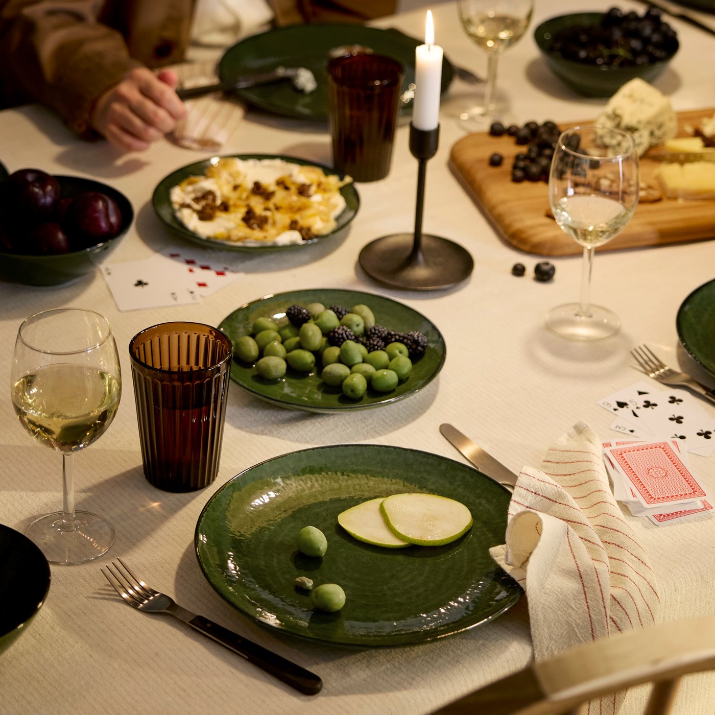 Les gens sont réunis autour d'une table pour un repas composé de fromage et de fruits frais, le tout dans une ambiance chaleureuse à la lueur des bougies.