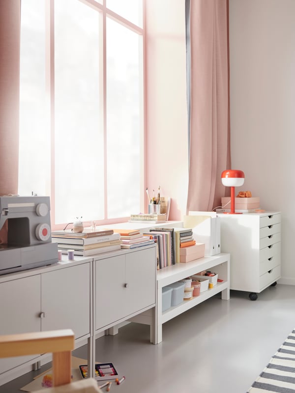 A grey LIXHULT cabinet, a white LACK TV bench and an ALEX drawer unit on castors side by side along a wall with a window.