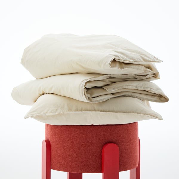 Close-up of a white set of ÄNGSLILJA duvet and pillowcase, piled on top of a red stool.