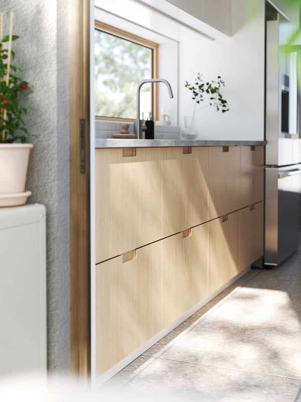 A patio door is open leading into a kitchen with stone floors. The bottom cabinets have FRÖJERED fronts made from bamboo.