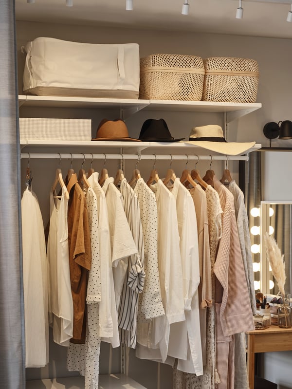 An open BOAXEL wardrobe with clothes hanging on a clothes rail. Hats and baskets sit on shelves above the hanging clothes.