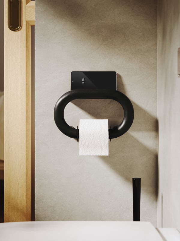 BÄSINGEN držač rolni toalet-papira boje antracita postavljen je na zid kupatila blage bež boje, a na njemu je rolna toalet-papira.