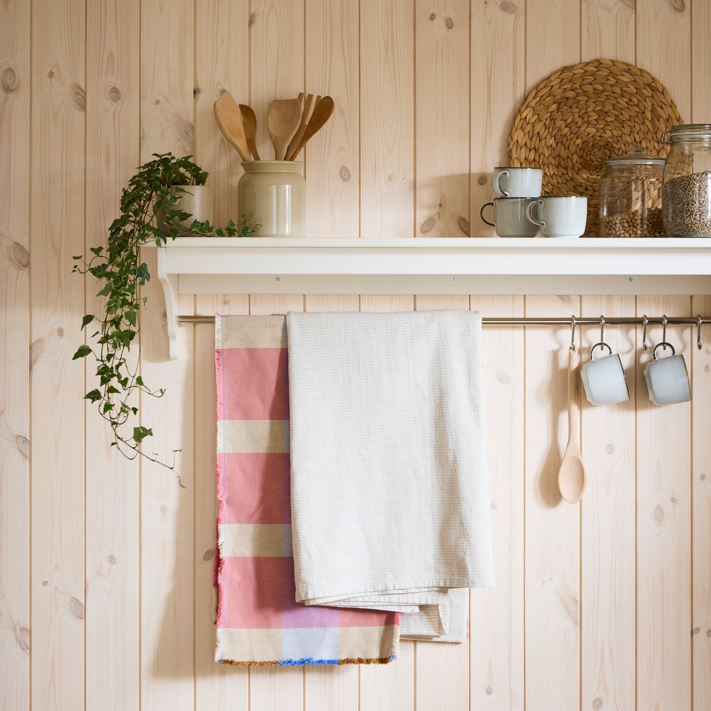 An off-white TORNVIKEN wall shelf is attached to a wall and a SILVERARV tablecloth and a table runner hang from its rail.